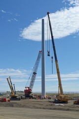 Wall Mural - A crane lifts a wind turbine blade into place with a clear sky behind. Workers guide the blade as other turbines are under construction