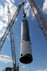 Wall Mural - The nacelle of a wind turbine is being lifted onto a tower by a crane. Nearby, other turbine components are visible