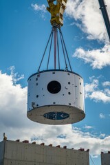 Wall Mural - The nacelle of a wind turbine is being lifted onto a tower by a crane. Nearby, other turbine components are visible