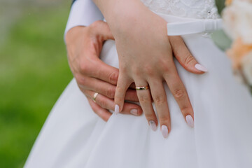 Wall Mural - A bride and groom are embracing each other with their hands on their hips. The bride is wearing a white dress and the groom is wearing a gold ring