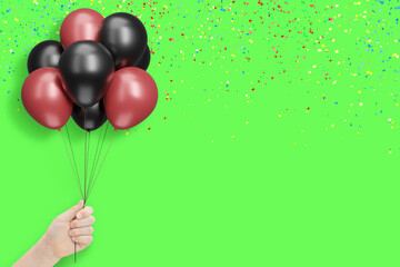 Aufkleber - Female hand holds bunch of red and black balloons on green background with confetti. Empty space for text