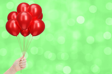 Aufkleber - Female hand holding bunch of shiny red balloons on blurred summer green background. Empty space for text