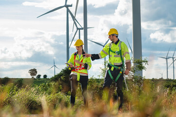 two men in safety gear are walking through a field of wind turbines