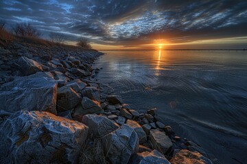 Poster - A serene scene of a sunset over a body of water with rocks in the foreground, perfect for use in travel or nature-related projects