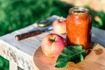 Glass jar of apple jam and fresh fruits on garden background.