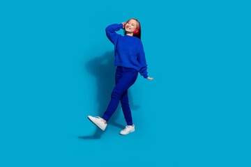 Canvas Print - Photo of chinese girl wear trendy pullover dancing meloman in wireless bluetooth earphones boogie woogie isolated on blue color background