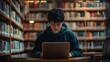 © Teerapat - Young Man Using Laptop in Library with Bookshelves in Background