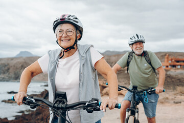 Canvas Print - Senior couple riding bikes together in rocky beach enjoying outdoor. Active mature people talking holding mountain bikes. Bicycle lifestyle concept, having fun.