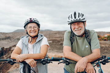 Canvas Print - Portrait of couple of old and happy in love seniors looking at the camera smiling and having fun with their bikes in the nature outdoors together feeling good and healthy.