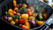 © munirahsamsudin - A variety of colorful, roasted vegetables being pulled out of an air fryer basket, with the steam rising