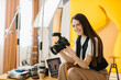 © dsheremeta - Portrait of a studio photographer at work. A beautiful brunette woman holds a professional camera in her hands and smiles.