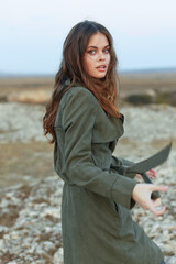 Wall Mural - Serene woman in green trench coat embracing nature on rocky hilltop in peaceful solitude