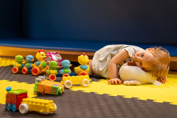 tired sleepy toddler girl playing at beautiful daycare center with toys. concept of daycare for babi