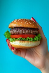 Wall Mural - Hand holding a fresh burger with lettuce and tomato against a blue background