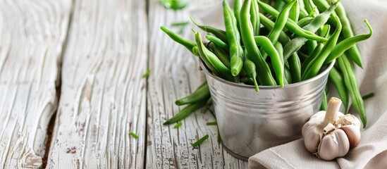 Canvas Print - Green beans in an aluminum cup along with a napkin and garlic on a white wooden table Autumn recipes Copy space