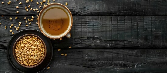 Canvas Print - Plate of roasted barley alongside a cup of hot Japanese barley tea or mugicha on a black wooden table. Copy space image. Place for adding text and design