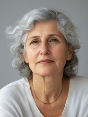 Aufkleber - A thoughtful mature woman with curly gray hair sits calmly, gazing softly at the camera, dressed in a cozy light sweater, in a serene indoor setting. Generative AI