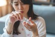 © miss irine - Young Asian woman takes a pill from a blister pack for stomach pain and headache relief. Close-up of her hand holding the tablet. She is taking medicine for treatment at home.