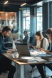 © miss irine - Modern office space with three individuals working together on laptops surrounded by books, papers, plants, and natural light from large windows creating a productive atmosphere.