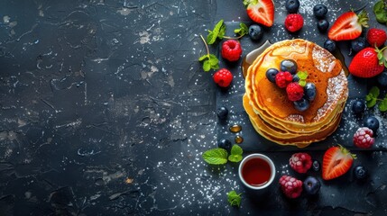 Top view of a stack of pancakes with maple syrup and fresh berries on a dark rustic surface