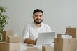 © alsu0112 - A young Hispanic man, an online store specialist, sits at a table with a laptop, surrounded by boxes of products, on a white background