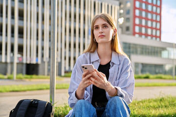 Young serious female using smartphone, modern city background