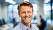 © Man888 - A middle-aged man with short brown hair and a friendly smile poses for a professional profile picture against a blurred office background.