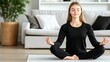 © lililia - A young woman sits cross-legged on a mat in her modern home, practicing yoga in black sportswear. With eyes closed, she embodies calmness and focus in her meditation