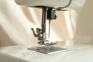 Poster - Sewing machine with beige thread on blurred background, closeup