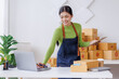 © David - Startup SME small business entrepreneur SME or freelance Asian woman standing using a laptop with box, online marketing packaging box and delivery, SME concept.