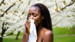 © LivaLife - Dark-skinned girl blowing her nose and sneezing into a handkerchief against a background of flowering trees. The concept of allergies, asthma