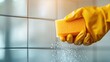 ©  Shomixer - A gloved hand holding a yellow sponge cleans tiled surfaces efficiently. The image emphasizes cleanliness, hygiene, and dedication to maintaining a spotless environment with attention to detail.