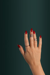 Female hand relaxed, long nails with red gel polish on an emerald green background. A woman with a classic stylish manicure and silver ring set