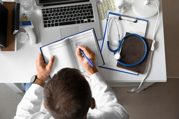 Canvas Print - Mature male doctor with notebook at desk in clinic, top view