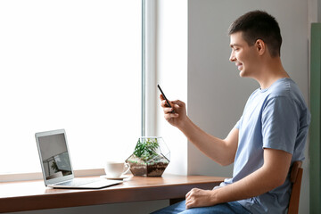 Canvas Print - Young man with smartphone near window