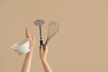 Wall Mural - Female hands holding colander, whisk and potato masher on brown background