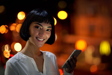 Poster - Phone, night and portrait of business woman in city for information, research and networking on deadline. Mobile, smile and face of creative writer, entrepreneur or employee on app on bokeh in Spain