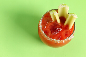 Glass of bloody mary with celery and salt on green background