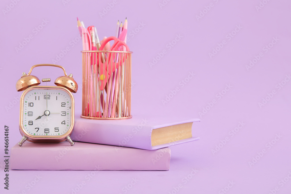 Alarm clock with books and stationery holder on lilac background