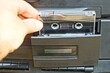 © FEDOR - one plastic old stereo with a recording audio cassette with magnetic tape is inserted by hand into a black electric tape recorder for musical playback