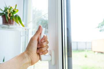 The hand holds the handle of a plastic double-glazed window, closing and opening the window with a rotary mechanism, the position of the handle for ventilation, micro-ventilation