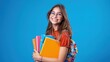 © farhan - Cheerful young woman with glasses, holding educational books, vibrant cobalt blue background, studio photo