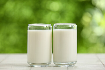 Glasses of fresh milk on white tile table outdoors