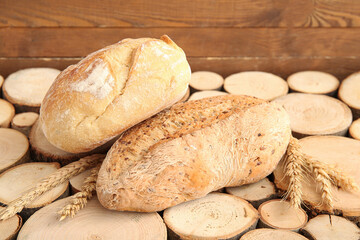 Loaves of fresh bread with wheat spikelets on wooden background