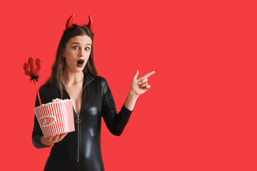 Sticker - Young woman dressed for Halloween with popcorn pointing at something on red background