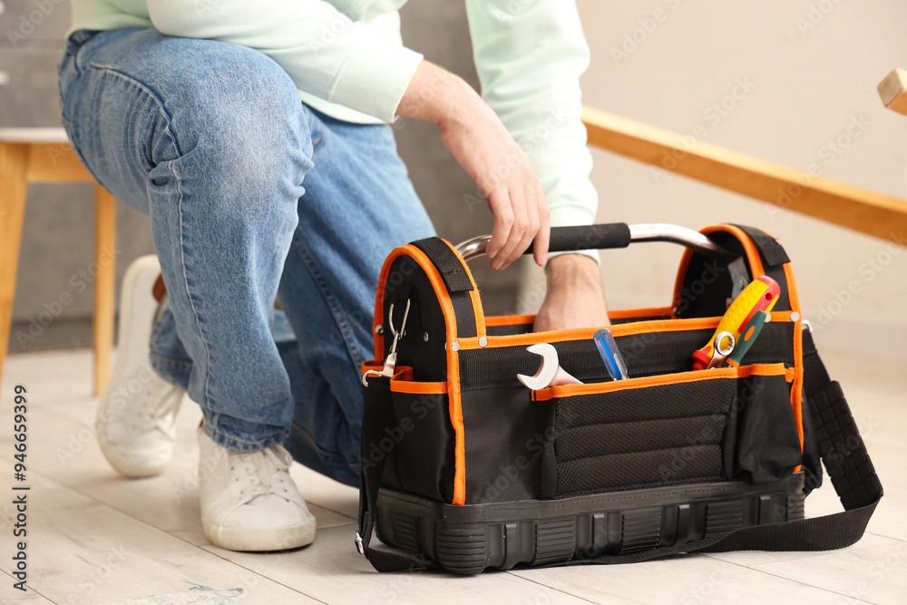Young man with bag of tools assembling furniture in kitchen, closeup