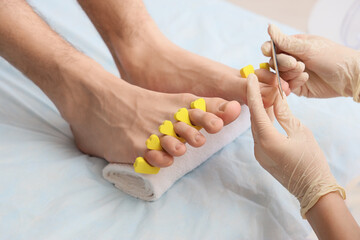 Wall Mural - Young man getting professional pedicure with toe separator and file on couch in spa salon, closeup