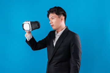 Wall Mural - Asian businessman in serious face checking through VR connecting to financial report in futuristic metaverse data analytics communication technology virtual reality at blue copyspace. Contrivance.