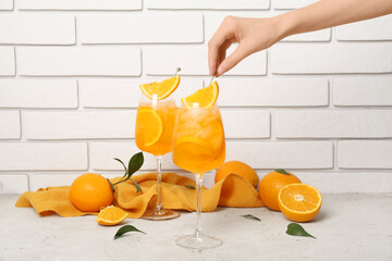 Wall Mural - Female hand with glasses of Aperol spritz cocktail and oranges on white table