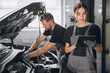© anatoliycherkas - Auto service, repair, maintenance concept. Mechanic checks the car at the service station. Charming woman and bearded engineer use tablet check car battery